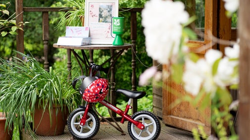 A bright red balance bike rests against a table at on the porch of the Welcome Hut at Rowallane Garden